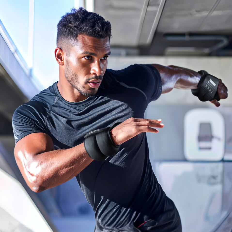 Man in a gym wearing black TRNR Wrist Weights and a black t-shirt.
